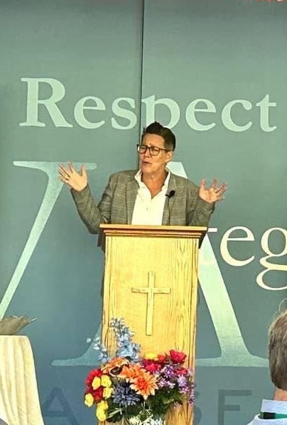 Pastor speaking with arms raised from behind podium